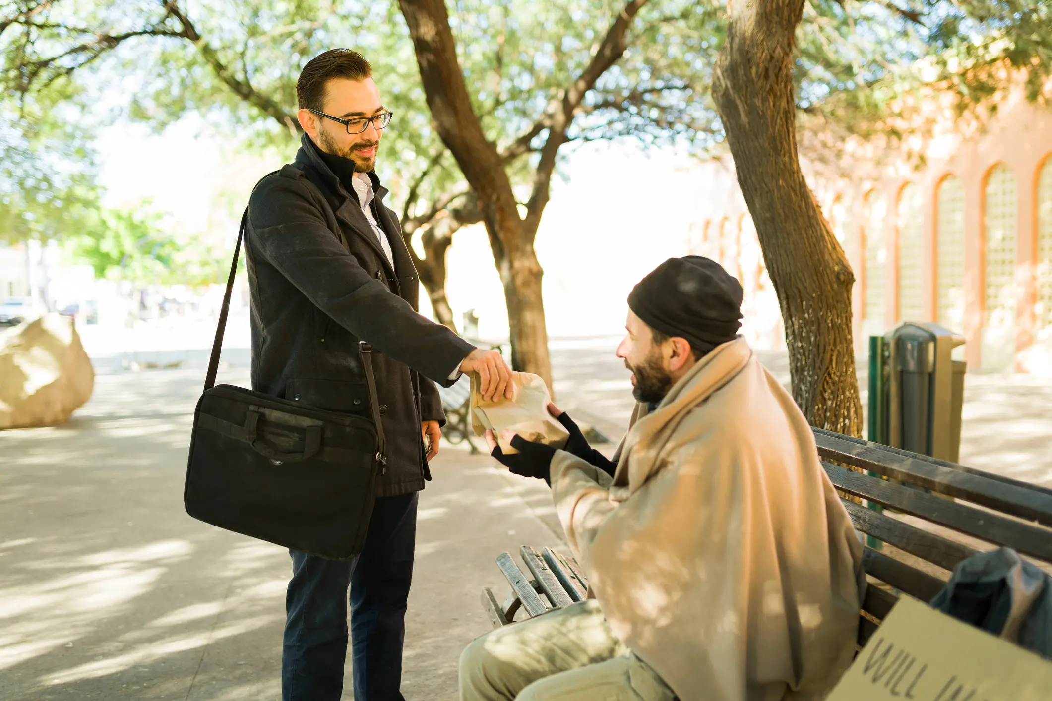 Man handing box to seated man on bench